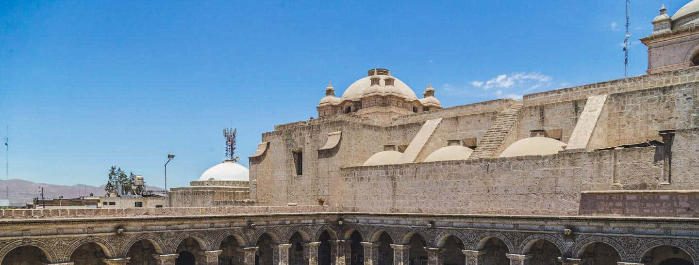 White building constructed using sillar (ash from the surrounding volcanoes). Blue skies and one white cloud visible in the top right of image.