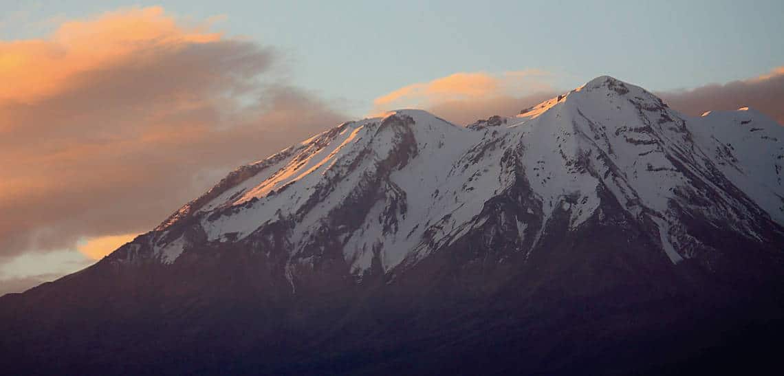 Snow-capped volcano. Blue sky with partial cloud cover.